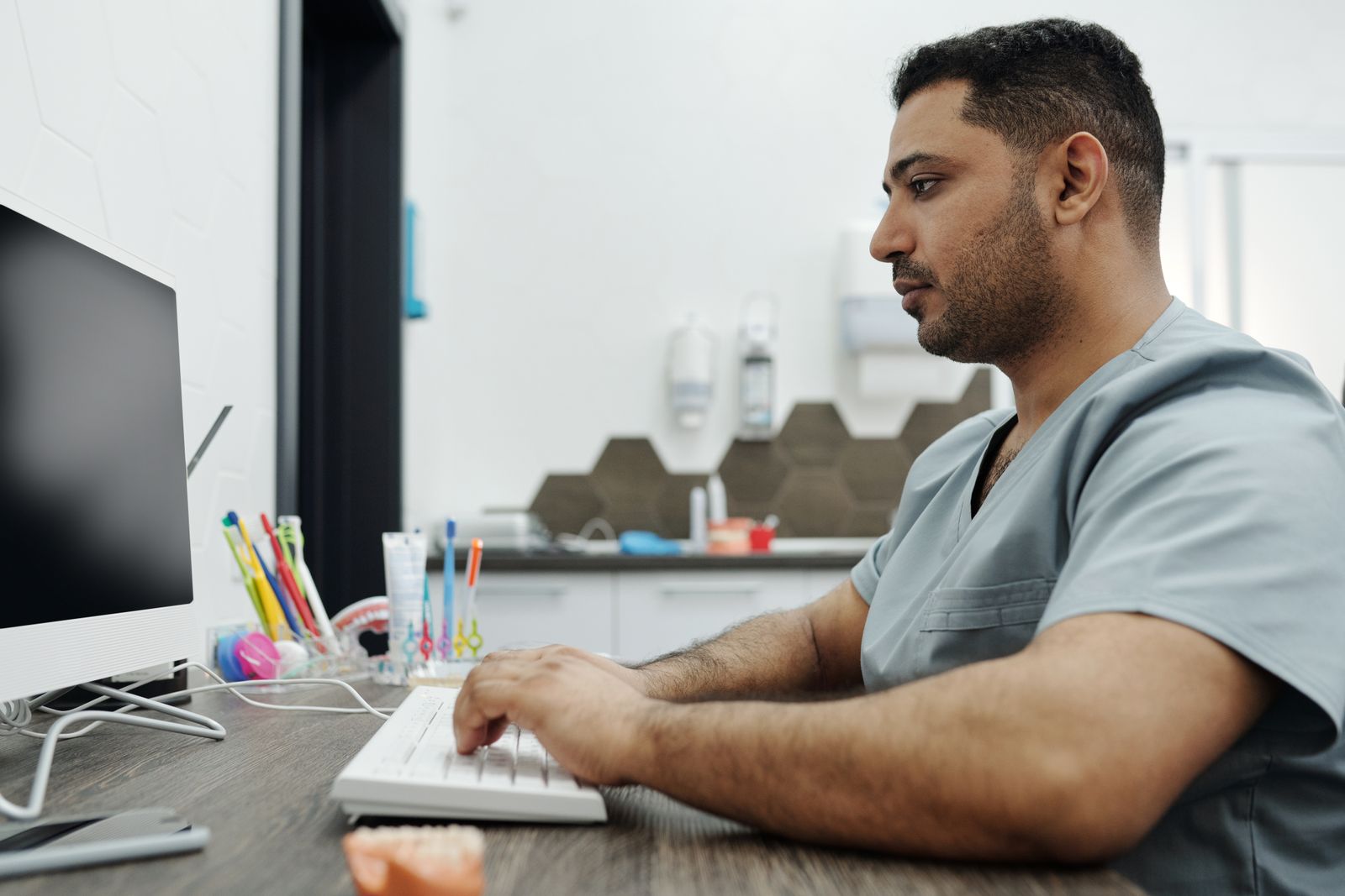 Zahnarzt in Praxiskleidung arbeitet am Computer an der Rezeption einer Zahnarztpraxis